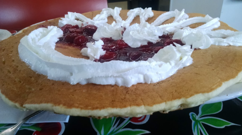 A large pancake topped with cherry filling and whipped cream, served on a colorful tablecloth.