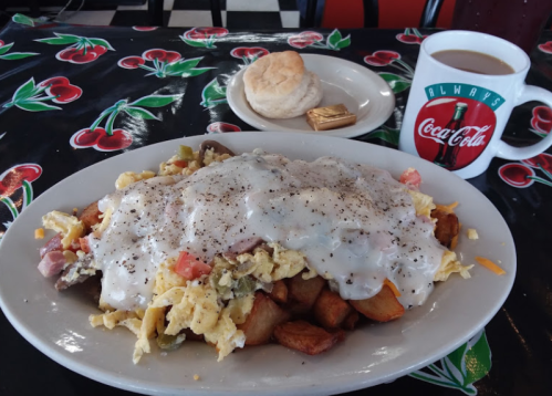 A hearty breakfast plate with scrambled eggs, potatoes, and gravy, served with a biscuit and coffee in a Coca-Cola mug.