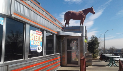 A diner with a large horse statue on the roof, featuring a sign for steak and eggs. Clear blue sky in the background.