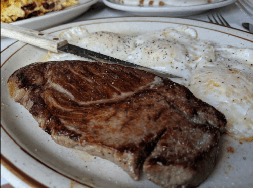 A plate with a juicy steak and two sunny-side-up eggs, garnished with pepper and a knife resting beside the steak.