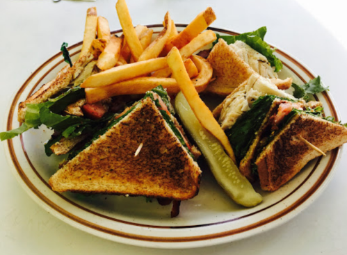 A plate of toasted sandwiches with lettuce, tomato, and a pickle, accompanied by golden French fries.