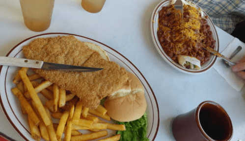 A plate with fried fish, fries, and a bun, alongside a bowl of chili topped with cheese.