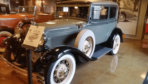 A vintage 1930s car displayed in a museum, featuring a green body, whitewall tires, and wire-spoke wheels.