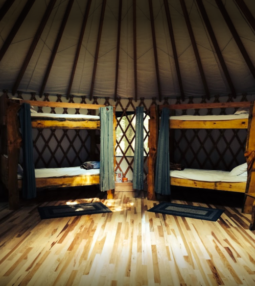 Interior of a yurt featuring two sets of wooden bunk beds and wooden flooring, with curtains for privacy.