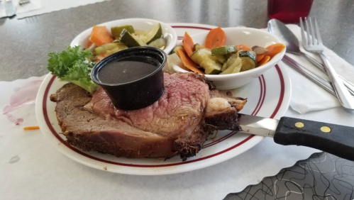 A plate with a slice of prime rib topped with a sauce cup, accompanied by mixed vegetables and a garnish of lettuce.