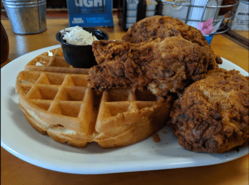 A plate featuring crispy fried chicken pieces alongside a golden waffle and a small cup of whipped cream.