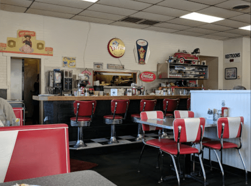 A retro diner interior with red and white booths, a counter with stools, and vintage decor on the walls.