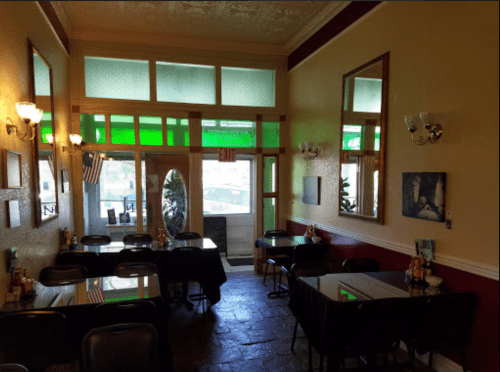 Cozy restaurant interior with tables, green accents, mirrors, and large windows letting in natural light.