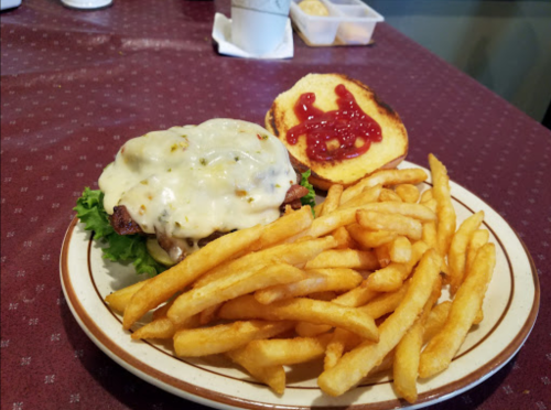 A plate with a cheeseburger topped with melted cheese and lettuce, served with a side of golden French fries and ketchup.