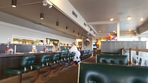 Interior of a restaurant featuring green booths, a long counter, and a few patrons. Bright and spacious atmosphere.