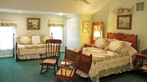 Cozy bedroom with two beds, a rocking chair, and soft green decor, featuring natural light and floral patterns.
