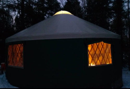 A lit yurt at dusk, surrounded by trees, with warm light glowing from its windows.