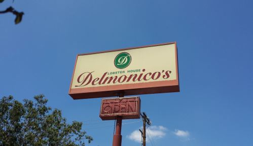 Sign for Delmonico's Lobster House with "OPEN" displayed, set against a clear blue sky.