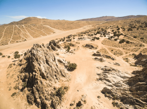 A rocky landscape with sparse vegetation and dirt roads under a clear blue sky.