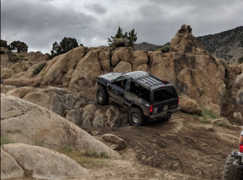 A black SUV navigating rocky terrain under a cloudy sky.