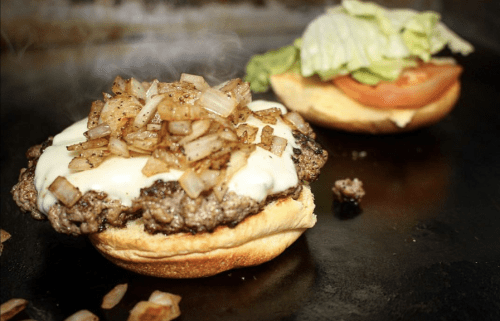 A juicy burger topped with melted cheese and sautéed onions, next to a bun with lettuce and tomato.