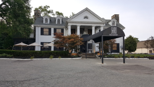 Exterior of Shiro Restaurant, a large white building with a black awning, surrounded by trees and outdoor seating.