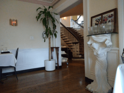 Interior of a restaurant featuring a potted plant, elegant staircase, and a decorative sculpture near dining tables.