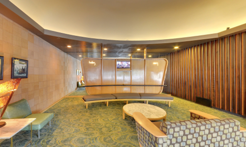 A modern lounge area with curved seating, a round table, and wooden accents, illuminated by soft lighting.