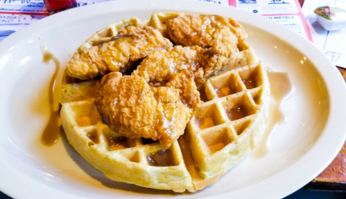 A plate of waffles topped with crispy fried chicken and drizzled with syrup.