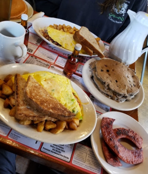 A breakfast spread featuring an omelette, toast, home fries, pancakes, sausage, and coffee on a table.