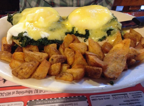 A plate of eggs Benedict with spinach and hollandaise sauce, served with golden-brown potato wedges.