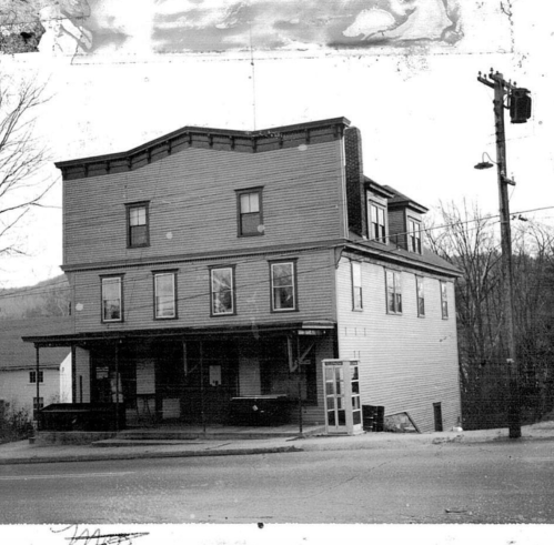 Black and white photo of a three-story building with a flat roof, featuring multiple windows and a porch.