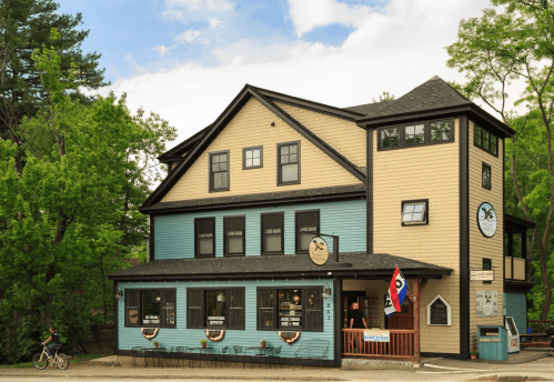 A charming multi-story building with a mix of blue and tan siding, featuring a welcoming entrance and outdoor seating.