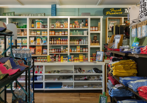 A colorful store display featuring shelves of food products, condiments, and clothing items in a cozy shop setting.