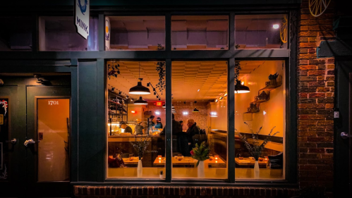 A cozy restaurant interior visible through large windows, with warm lighting and patrons enjoying their meals.