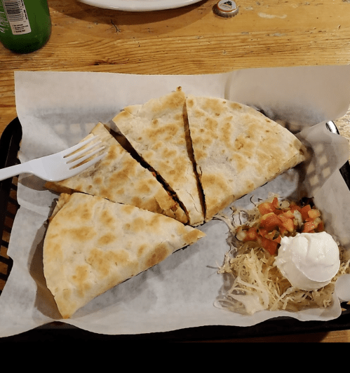 A plate with sliced quesadilla, topped with sour cream and accompanied by shredded lettuce and pico de gallo.