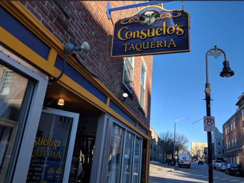 Sign for Consuelo's Taqueria on a brick building, with a clear blue sky and street view in the background.