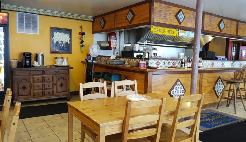 Cozy restaurant interior with wooden tables, a service counter, and colorful decor.