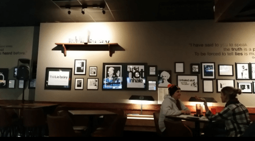 A cozy café interior with framed art on the walls and two people sitting at a table, engaged in conversation.