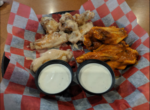 A platter of chicken wings with two dipping sauces, served on red and white checkered paper.