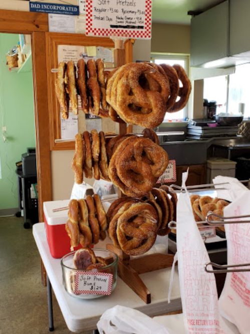 A display of soft pretzels hanging on a stand, with a sign indicating prices and options in a cozy shop setting.