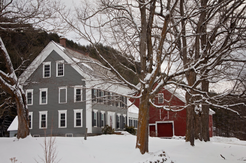 A gray and red house surrounded by snow-covered trees in a winter landscape.