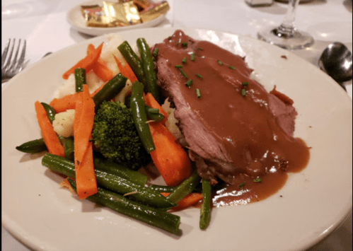 A plate of sliced roast beef with gravy, served alongside mixed vegetables and mashed potatoes.
