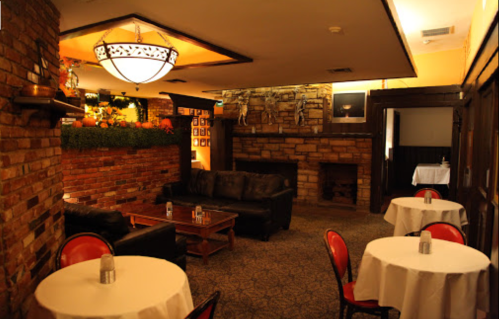 Cozy restaurant interior with brick walls, leather seating, and small tables, featuring a fireplace and warm lighting.