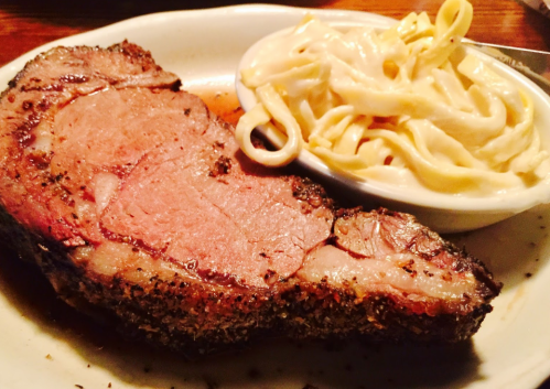 A plate featuring a juicy slice of prime rib alongside creamy fettuccine alfredo.