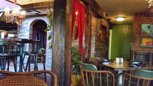 Cozy restaurant interior featuring wooden beams, red curtains, and a mix of tables and bar seating.
