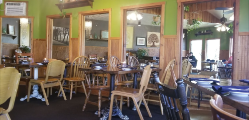 Cozy restaurant interior with wooden tables and chairs, green walls, and large windows letting in natural light.
