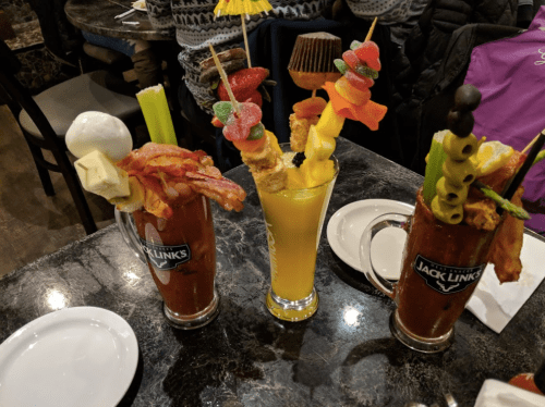 Three colorful drinks on a table: two Bloody Marys with garnishes and a fruity cocktail with a variety of toppings.