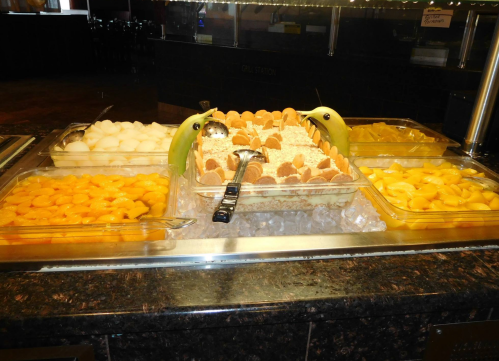 A dessert buffet featuring various fruits, ice cream, and a decorative display with bananas and ice.