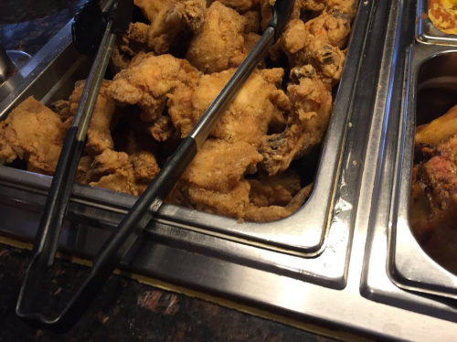 A tray of crispy fried chicken pieces with tongs resting on the side.