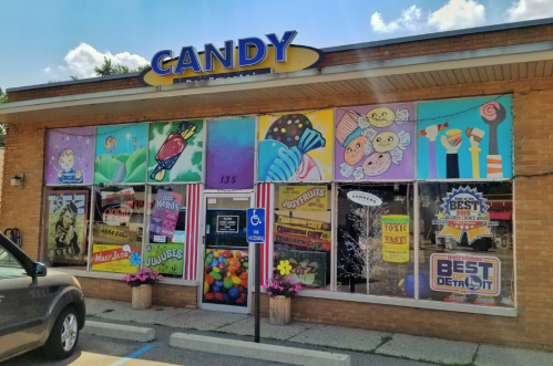 Colorful candy store exterior with vibrant murals, large windows displaying sweets, and a welcoming entrance.