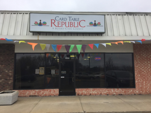 Exterior of Card Table Republic, a board game lounge, featuring colorful bunting and an "OPEN" sign.