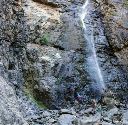 A waterfall cascades down rocky cliffs, with people exploring the area around the base among the boulders.