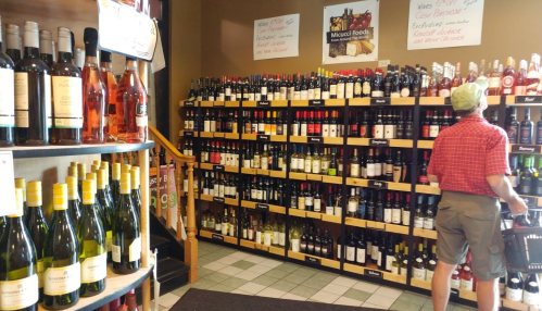 A person browsing a wine shop with shelves filled with various bottles of wine and a display of mixed foods.