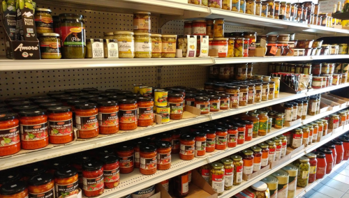 A grocery store shelf filled with various jars of sauces, pickles, and condiments in organized rows.